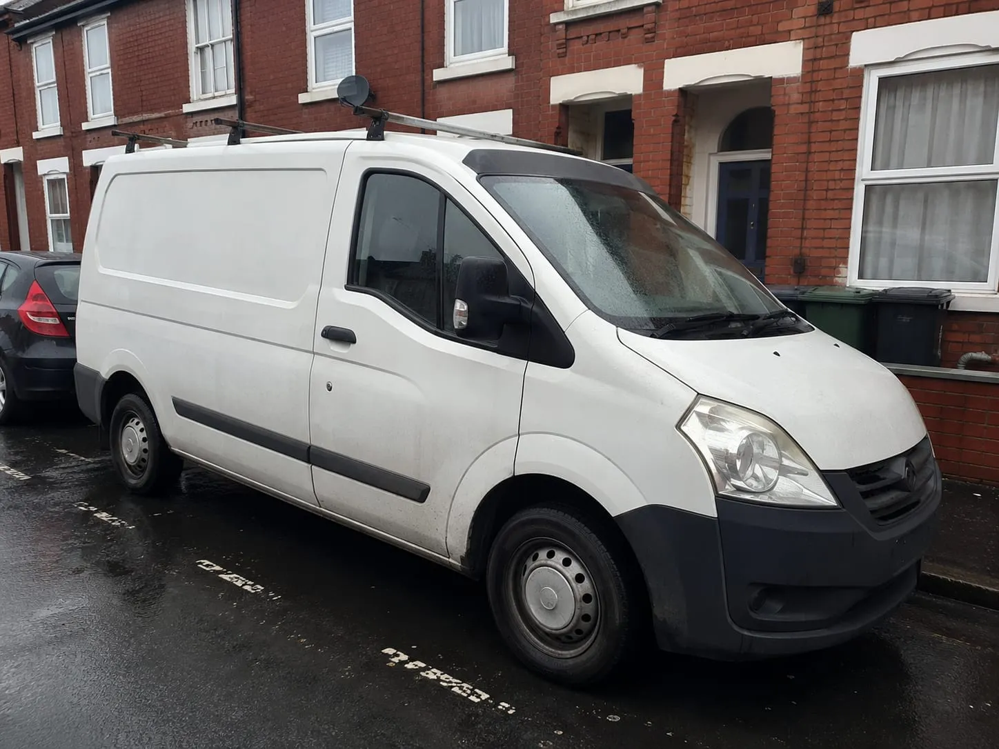 A plumber's white work van parked on a red-brick terraced street in Reading on a wet day